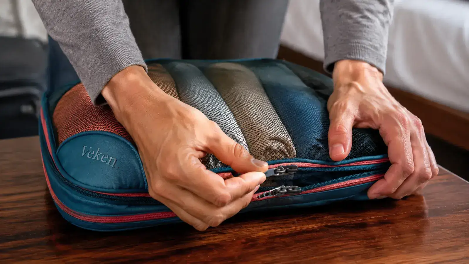 Hands pressing down on a compression packing cube zipper to squeeze air out of a cube filled with rolled t-shirts