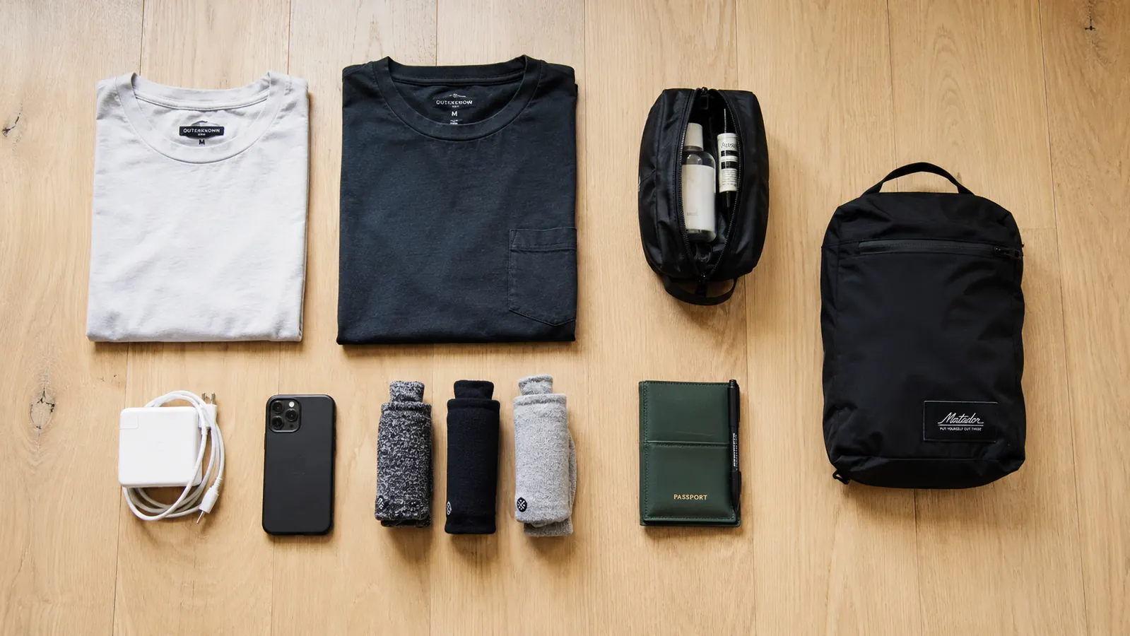 Overhead flat-lay of everything a traveler packs into a carry-on and personal item, including clothes, toiletries, electronics, and a folded daypack