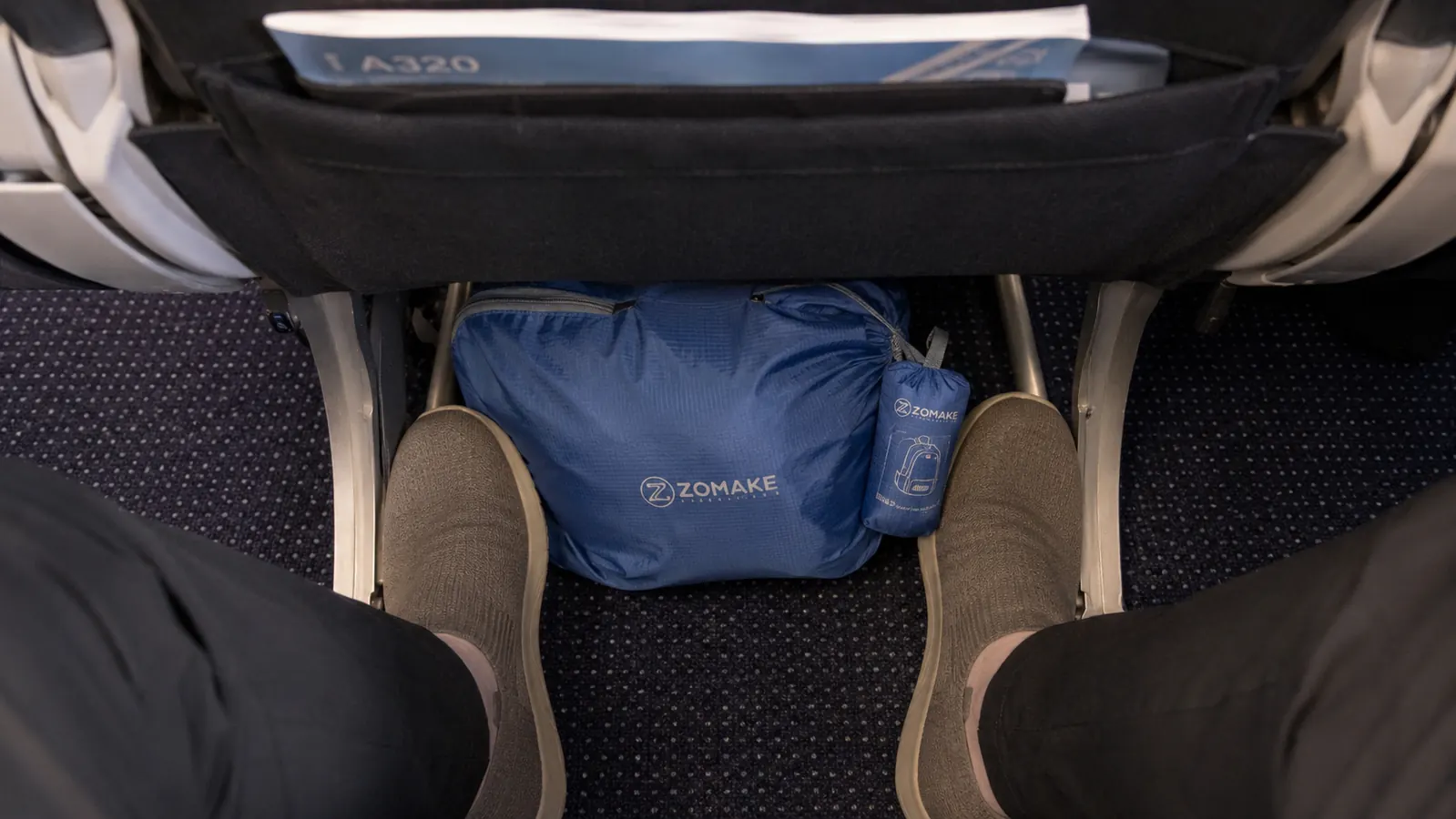 Packable daypack stored under an airplane seat alongside a pair of shoes and a water bottle