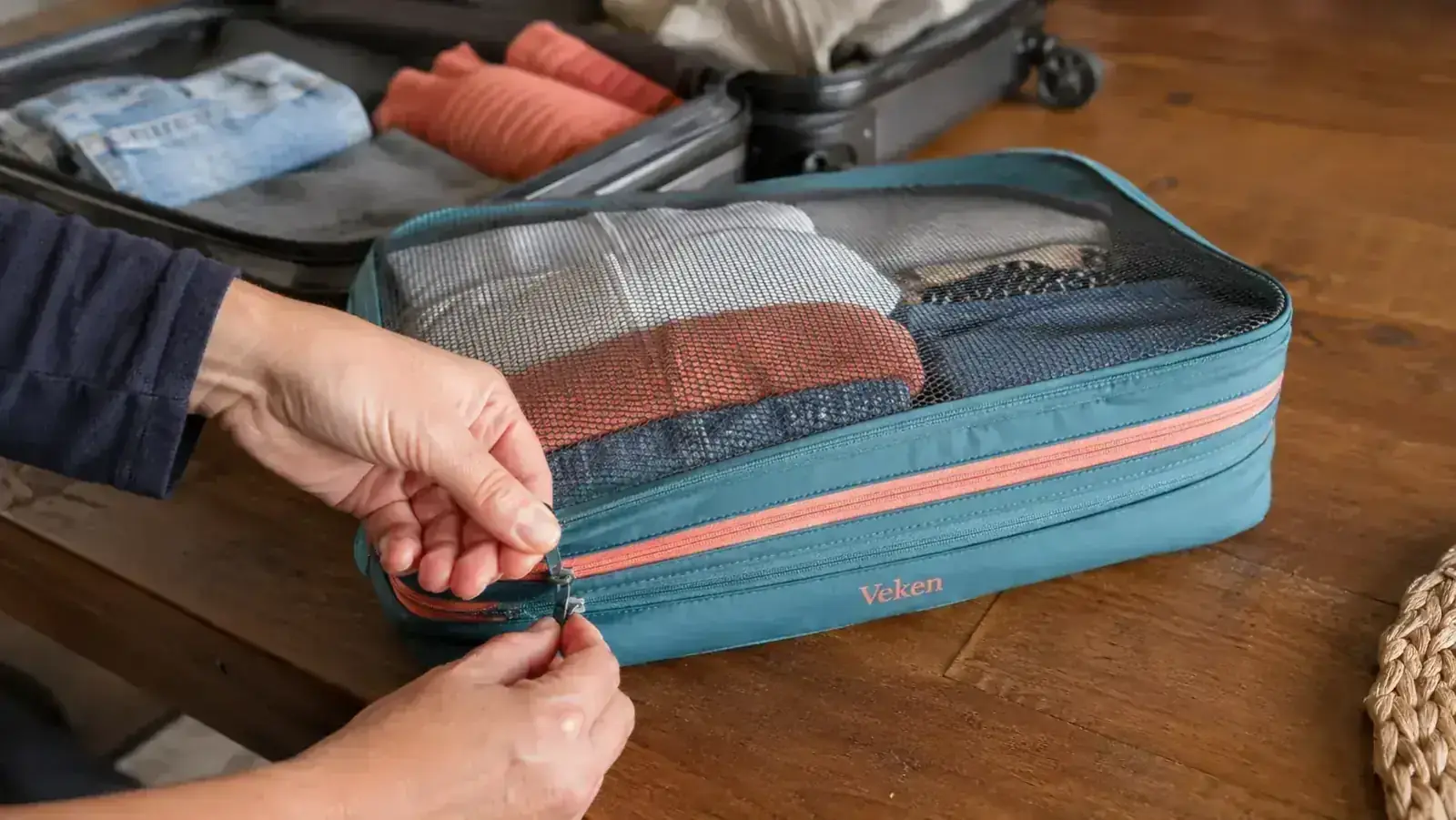 Hands pressing down the compression zipper on a fabric packing cube filled with folded t-shirts and jeans