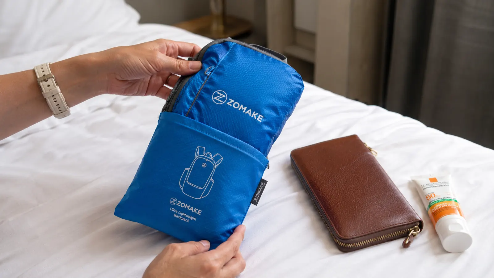 Packable daypack unfolded from its pouch on a hotel bed, travel essentials beside it